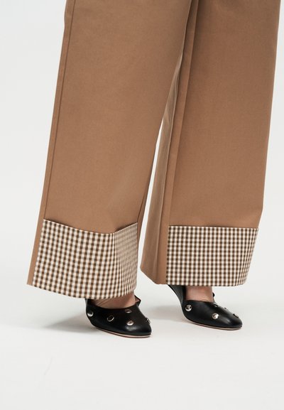 Καφέ παντελόνια με φαρδιά μπατζάκια και καρό μανσέτες σε καφέ και λευκό, φορεμένα με μαύρα slip-on παπούτσια με ασημένιες καρφίτσες.