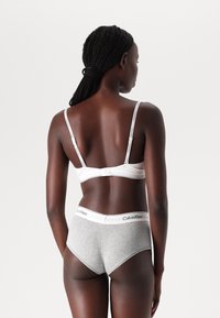 Calvin Klein hvit BH med justerbare stropper og grå bomullsbrief med logo-bånd, sett fra baksiden, som viser en jevn tekstur.