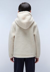 Krämfärgad fleecejacka med en fluffig textur, överdimensionerad huva och avslappnad passform. Bakvy visar inga synliga fästen eller detaljer.