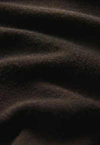 Blødt, mørkebrunt stof med subtil tekstur og blide folder fremhævet af dæmpet belysning.