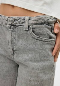 Vaqueros de mezclilla gris con una textura desgastada, que cuentan con un diseño clásico de cinco bolsillos, cierre de botón metálico y una cinturilla resistente.