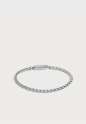 Bracelet chaîne torsadée en argent avec un fermoir cylindrique orné de motifs géométriques gravés, présenté sur un fond clair uni.