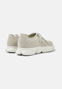 Helle beige Sneaker mit einem gestrickten Mesh-Obermaterial, runder weißer Gummisohle, Schnürverschluss und strukturierten Akzenten an der Ferse.