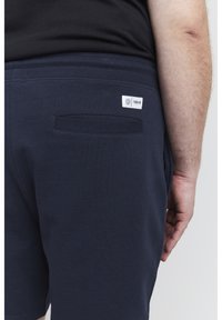 Dunkelblaue Shorts aus weichem Baumwollmischgewebe mit einer Gesäßtasche und einem gewebten Etikett. Der Bund ist elastisch für zusätzlichen Komfort.