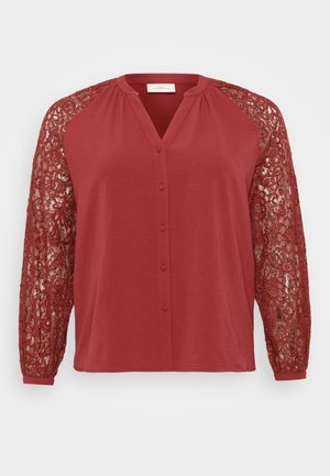 Red blouse with a front button placket, featuring long lace sleeves. Material is textured, with intricate lace patterns on sleeves.