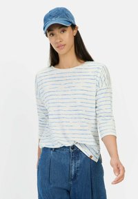 Lichte, gestreepte lange mouwen shirt in wit en blauw, gecombineerd met hoge taille, losse blauwe denim broek en een blauwe denim pet.