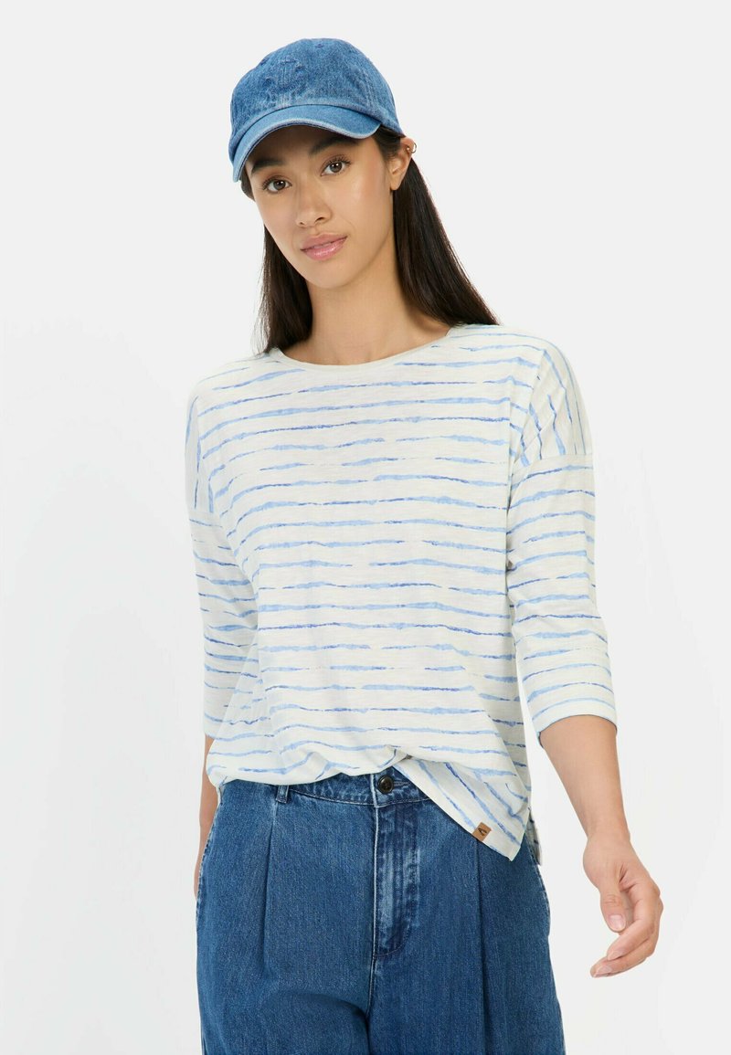 Lichte, gestreepte lange mouwen shirt in wit en blauw, gecombineerd met hoge taille, losse blauwe denim broek en een blauwe denim pet.