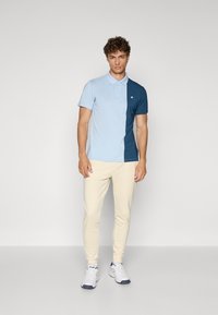Polo shirt in light blue and dark blue, cotton blend, short sleeves, button-down collar, emblem on chest, paired with cream joggers and white sneakers.