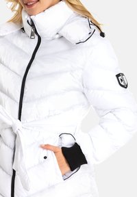 Weißer Pufferjacke mit diagonaler Steppung, hohem Kragen, verstellbarem Halsauschnitt, schwarzen Akzenten und einem gebundenen Gürtel in der Taille. Verfügt über Seitentaschen.