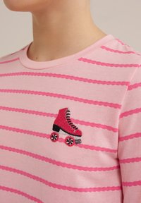 Pruhované růžové bavlněné tričko s krátkým rukávem, které na levé části hrudníku zdobí červený vyšívaný design kolečkového bruslení.