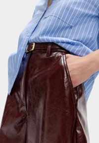 Niebieska koszula w paseczki o luźnym kroju, zestawiona z wysokimi, bordowymi skórzanymi spodniami z widocznym paskiem i detalami kieszeni.