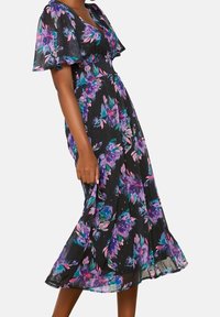 Svart blommig klänning med korta volangärmar, prydd med lila och rosa blommor; lätt och flödande material, knälång design.