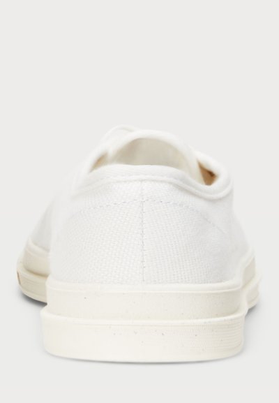 Λευκά καμβά sneakers με υφή στην επάνω πλευρά, καουτσούκ σόλα και στρογγυλή μύτη. Στην πλάτη φαίνεται �μια λεία φτέρνα και ελάχιστες ραφές.