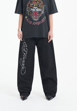 Zwarte oversized t-shirt met een kleurrijke tijgerafbeelding en de tekst "LOS ANGELES", gecombineerd met wijde zwarte denimbroek met rhinestone-details.