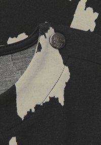Tkanina w czarno-białe wzory o fakturowanym wyglądzie, z czarnym guzikiem z wygrawerowanym napisem "Street One" w okolicy dekoltu.