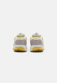 Sapatilhas Nike com um esquema de cores branco, cinza e amarelo; apresentam material em malha, detalhes triangulares e uma sola texturizada para aderência.