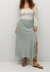 Lange, lichtgroene rok met een bloemenpatroon, voorzien van een zijsplit. Gepaard met een witte off-shoulder blouse en bruine sandalen met bandjes.