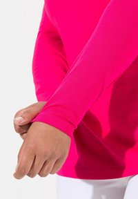 Dlouhá rukávová košile v živě růžové látce, hladká textura, přiléhavý design, který se vyznačuje těsným manžetou, na které je ruka upravující rukáv.