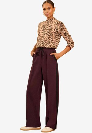 Top de manga larga con estampado de leopardo, cuello alto; pantalones anchos burdeos con bolsillos laterales y franjas negras en los lados; combinados con zapatos beige.