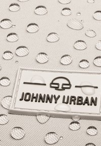 Vízhatlan szövet látható vízcseppekkel; texturált mintázattal rendelkezik. A kiemelkedő domború címke fekete színnel olvashatóan a "JOHNNY URBAN" feliratot viseli.