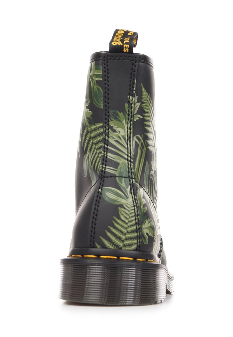 Schwarzer Lederstiefel mit grünen botanischen Blattmustern, dick profillierter Sohle, gelber Naht und einer Lasche mit gelbem Text.