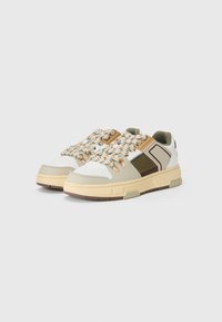 Sneakers feature a white, beige, and olive green design, with a textured patterned upper and braided laces, on a chunky, beige sole.