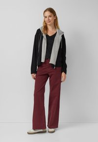 Zwart en grijs zip-up hoodie gelaagd over een zwart v-hals top, gecombineerd met bordeaux brede broek en crèmekleurige instappers.
