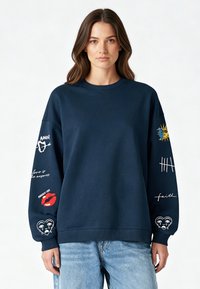 Felpa navy con maniche lunghe, caratterizzata da diversi design ricamati colorati sulle maniche, inclusi testo e simboli. Tessuto morbido e strutturato.