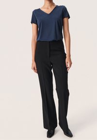 Námořnické tričko s výstřihem do V v kombinaci s černými kalhotami s vysokým pasem, které se vyznačují hladkým materiálem a rovnými nohavicemi. Obuv je černá.