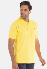 Polo shirt jaune à manches courtes en coton, avec un col et un petit logo noir sur le côté gauche de la poitrine, design uni sans motifs.