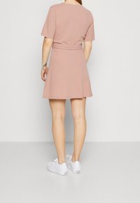 Krátké růžové šaty s krátkými rukávy, vypasovaným pasem, rozevlátou sukní a hladkým povrchem, doplněné bílými teniskami.