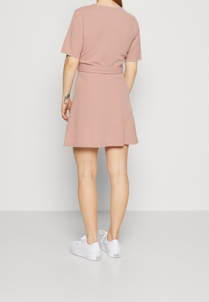 Krátké růžové šaty s krátkými rukávy, vypasovaným pasem, rozevlátou sukní a hladkým povrchem, doplněné bílými teniskami.