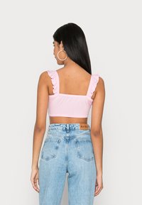 Top cropped rosa claro com alças de babados, combinado com jeans azul claro de cintura alta. Textura do tecido suave com um design ajustado.