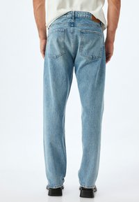 Jeans de mezclilla azul claro con un corte holgado, que cuentan con dos bolsillos traseros, costuras visibles y un parche de cuero marrón en la cinturilla.
