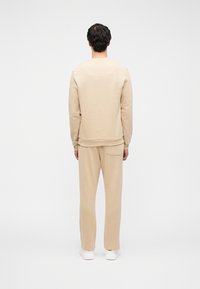 Μπεζ φούτερ και παντελόνι από απαλό ύφασμα, με άνετη γραμμή και απλό σχέδιο, σε προβολή από πίσω.