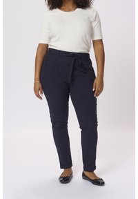 Marine bukser med knyttet talje, forlommer, tætsiddende ben og oprullede manchetter, parret med en tætsiddende, kortærmet hvid top og sorte flade sko.