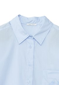 Jasnoniebieska koszula z krótkim rękawem, z kołnierzykiem typu spread i kieszonką na piersi z wyszywanym motywem liścia. Gładka tekstura materiału.
