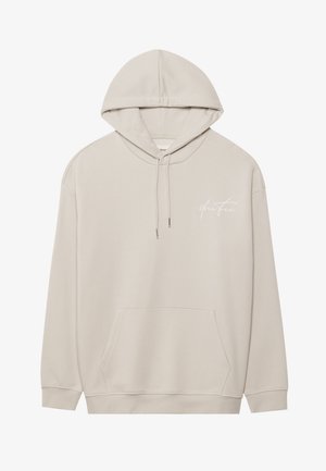 Sudadera beige de tela suave, con un bolsillo canguro en la parte frontal, capucha con cordón y un logo en cursiva blanca en el lado izquierdo del pecho.