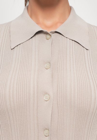 Close-up of a beige ribbed knit top with a wide collar and four matching buttons down the center front.