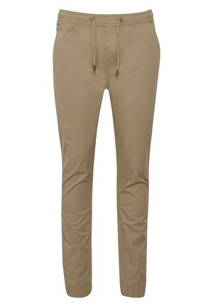 Pantalons de jogger beige en tissu doux, dotés d'une taille élastique avec cordon de serrage et d'ouvertures de jambe fuselées. Texture lisse, sans motifs.