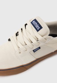 Beige nubukist ja kanvasest sneaker, millel on karamellpruun tall, kreemjad nöörid ja tumblue Etnies brändi sildid keelel ja külgpanelil.