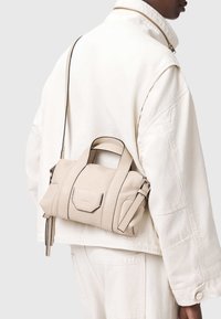 Beige leren handtas met een gestructureerde afwerking, voorzien van twee handvatten en een verstelbare riem. Minimalistisch ontwerp met subtiele stikseldetails.