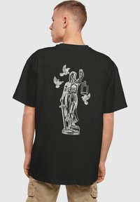 Schwarzes T-Shirt mit einem silbernen Grafik eines in Gewänder geh�üllten Figures, der Waagen hält und von fliegenden Vögeln umgeben ist, aus Baumwolle.