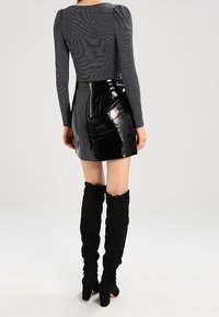 Svart lackläder mini kjol med dragkedja, matchad med en grårandig långärmad topp med puffade axlar. Knähöga svarta stövlar.