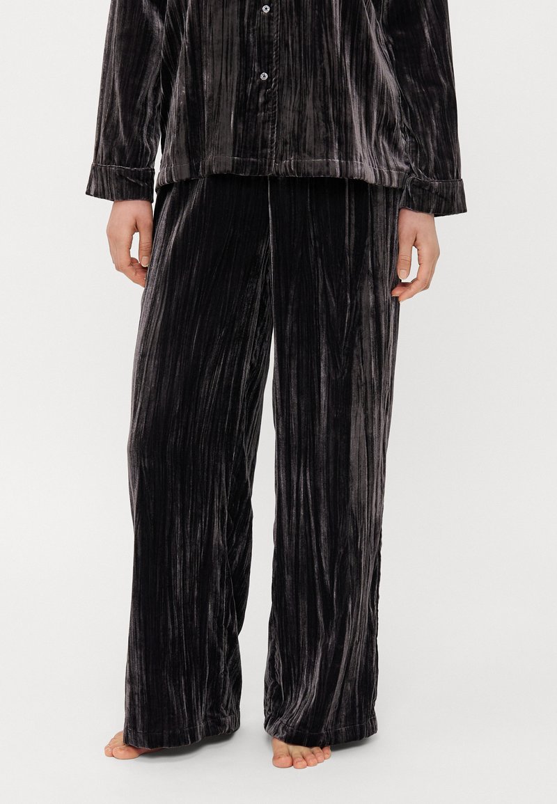 Velvet pyjama set in donkergrijs met verticale strepen. Geïntegreerde knoopsluiting aan de bovenkant en losvallende broek. Zachte textuur, lange mouwen en brede pijpen.