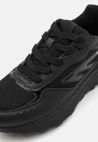 Black athletic shoe featuring a combination of mesh and synthetic leather. It has a textured surface, round laces, and a cushioned sole.