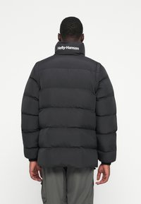 Schwarze Puffjacke mit hohem Kragen und horizontal ge quiltetem Design. Markenlogo auf dem Kragen. Weiche, matte Textur.