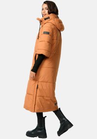 Oranje pufferjas met een capuchon, tot op de knie, met korte mouwen en een ritsluiting aan de voorkant. Zwarte rubberen laarzen tot de knie.