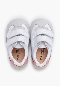 Zapatillas infantiles blancas y grises con dos correas de Velcro, punta redondeada, textura suave y acentos rosas en el lateral. Nombre de la marca visible en el interior.