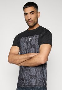 Μαύρο αθλητικό μπλουζάκι με υφή εμπρός μέρους σε σχέδιο φιδιού σε αποχρώσεις του γκρι. Κοντά μανίκια με εφαρμοστή σχεδίαση και διακριτικό λογότυπο.